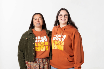 Two models smiling while wearing the MORE DOEY, LESS HUI hoodie, a unisex Māori clothing piece made for Kiwis who love comfort and effortless style.