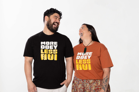 Two models laughing while wearing the MORE DOEY, LESS HUI T-shirt, a unisex Māori clothing piece made for Kiwis who love comfort and effortless style.